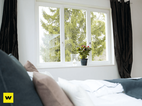 Modernes Schlafzimmer mit großem Fenster, Vorhängen und Zimmerpflanze auf Fensterbank.