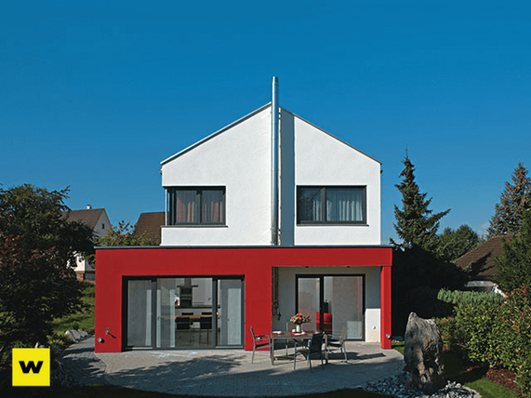 Modernes Einfamilienhaus mit roter Fassade und großem Garten bei sonnigem Wetter.