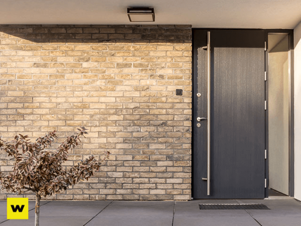 Moderne Haustür aus dunklem Material in Backsteinfassade mit seitlichem Glaselement.